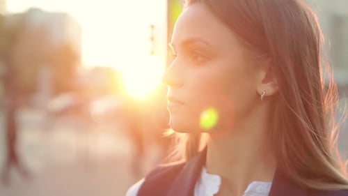 Young attractive girl in the center of the city, looking into the distance at sunset in the evening