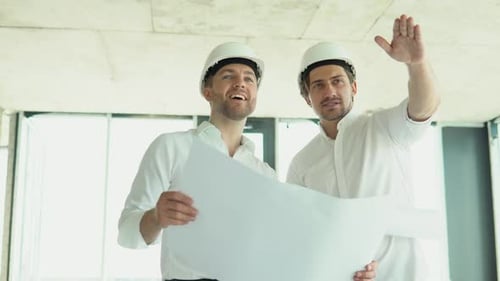 Um jovem engenheiro em capacetes de segurança em pé em um prédio em construção segurando uma planta de