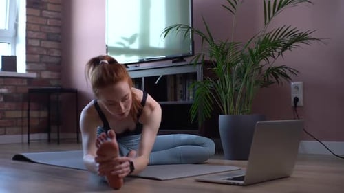 Portrait of Sporty Young Woman Doing Stretching Exercise on Yoga Mat Watching Video Online on Laptop