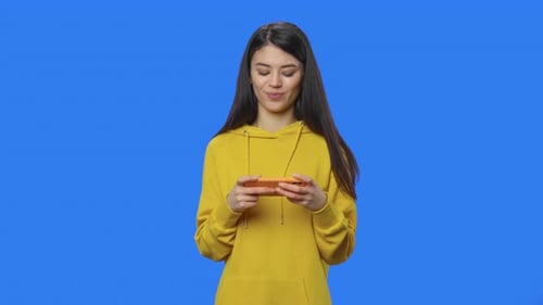 Woman Playing Game on Phone Against Blue Background