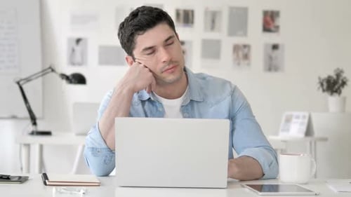 Tired Young Adult at Desk with Laptop