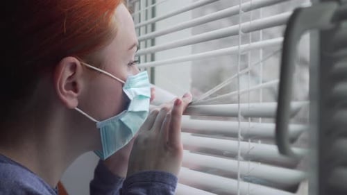 Red-Haired Woman in Mask Peers Out Window