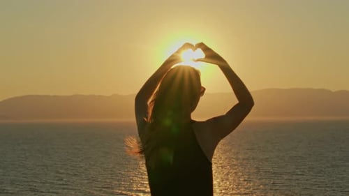 Woman Silhouetted Making Heart Shape at Golden Sunset