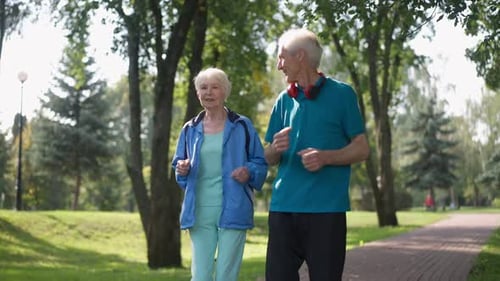 Smiling Senior Caucasian Couple Jogging in Slow Motion in Sunny Park