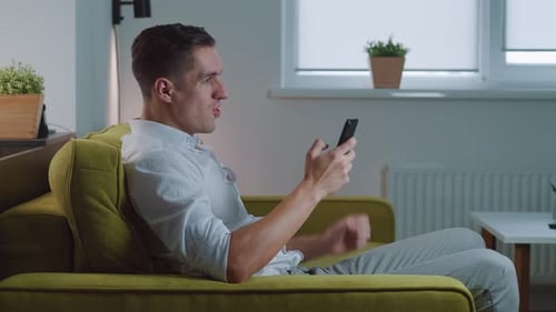 Excited man cheers success using mobile phone indoors