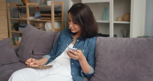 Woman Sitting on Couch Writing in Notebook