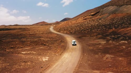 One White SUV Car Driving Alone Travel on Empty Dirt Road Freeway Through Desert Volcanic Landscape