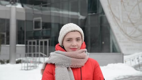 Hipster Girl Face in a Knitted Hat Straightens a Scarf and Collar Standing on the Street