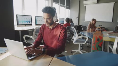 Young Man in Headphones Working on Laptop in Office