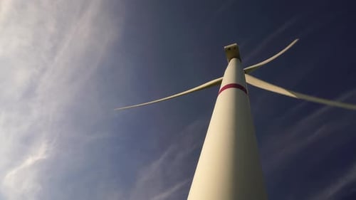 Blätter einer großen Windkraftanlage in einem Feld vor dem Hintergrund eines wolkenblauen Himmels am Horizont