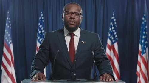 Man Gives Speech at Podium with Flags