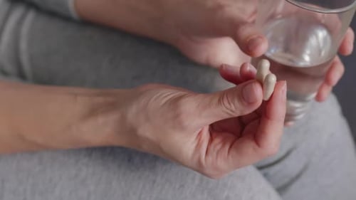 Close-up of a Woman Holding a Vitamin Supplement Pills and a Glass of Water