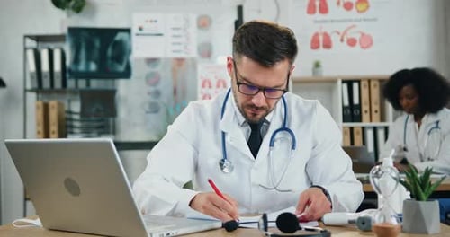 Docteur en lunettes travaillant avec des documents médicaux et dactylographiant sur ordinateur dans le bureau de la clinique