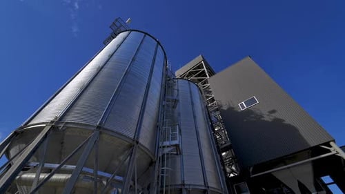 Silver containers outside. Modern agricultural complex against blue sky. Large grain elevators.