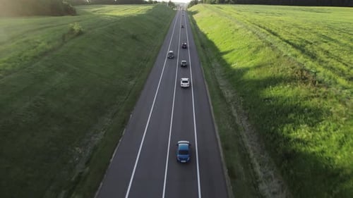 Cars drive one by one along a beautiful country road in the summer during sunset.