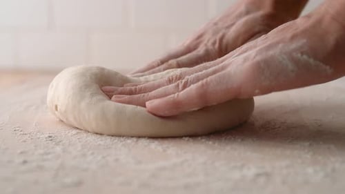 Die Kamera folgt den Händen eines Mannes beim Kneten eines Teigs. Zeitlupe.