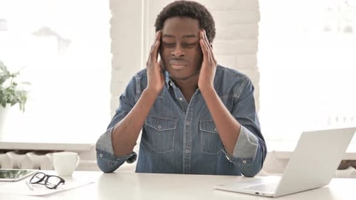 Man Rubs Temples Suffering from Headache at Desk