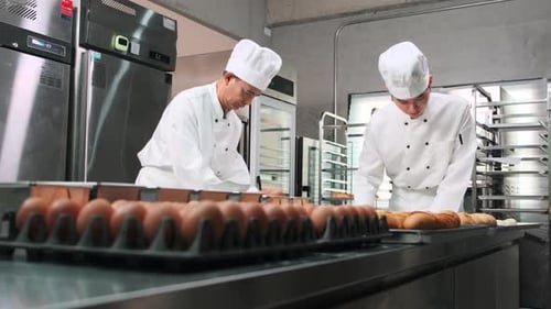 Asian male chefs in uniforms are preparing to bake bread in a stainless kitchen.