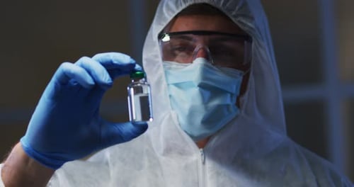 Caucasian male medical worker wearing protective clothing mask and gloves holding vaccine vial in la