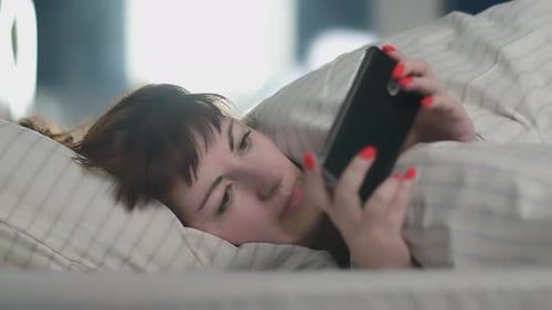 Woman Using Smartphone in Bed, Relaxing Indoors