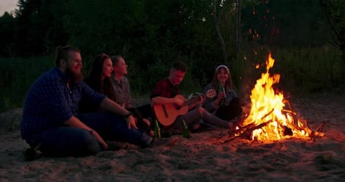 Friends Gather Around Bonfire on Beach at Night