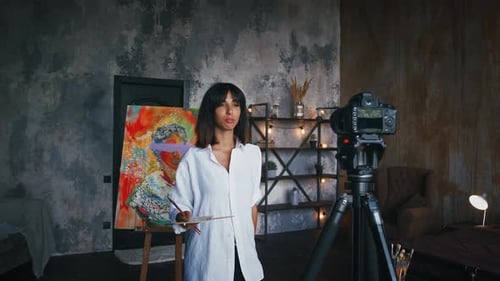 Mujer pintora posando cerca de un retrato en estilo de arte moderno contra cámara fija en trípode y