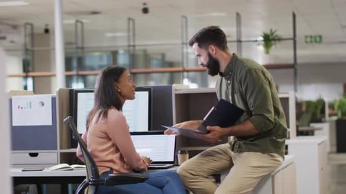 Video of diverse businesswoman and businessman using laptop and talking in office