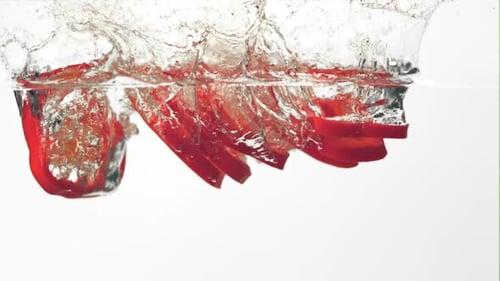 Super Zeitlupe Motion-Stücke roter Paprika fallen mit Spritzern ins Wasser