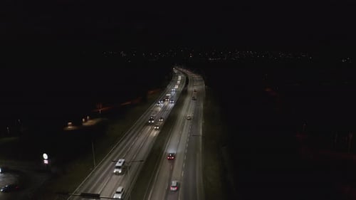 Cars driving at night on illuminated highway. Steady drone shot.