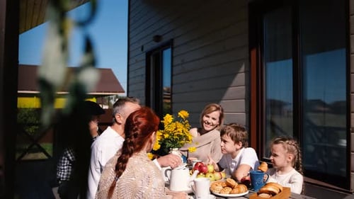 Family Members of Several Generations Sit at a Wooden Table on the Terrace Outside the House and