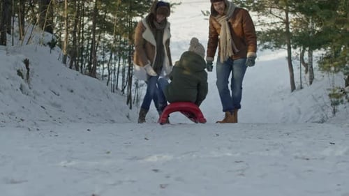 Casal correndo atrás de criança andando de trenó ladeira abaixo
