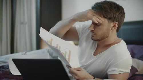 Man Analyzes Charts in Bed with Laptop