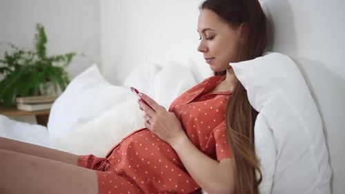 Pregnant Woman Resting with Smartphone in Bedroom