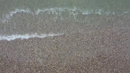 The spray from the wave that came to the shore and hit the rocky beach.