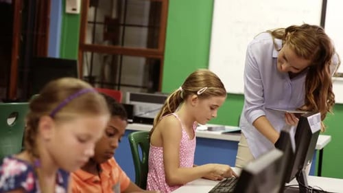 Teacher assisting school kids on personal computer in classroom