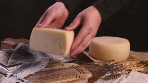 Women hands put pieces of fresh homemade cheese on a wooden board close up