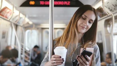 Happy Relaxed Beautiful Millennial Girl Stands in Subway Train Looking at Smartphone Using