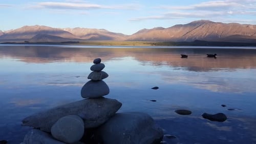 Zen stone and mallard ducks swim at Lake Tekapo, South Island