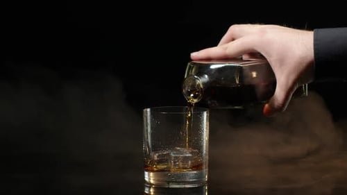 Hand Pours Whiskey into Glass with Ice