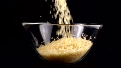 Uncooked Rice Grains Falling Into a Glass Bowl