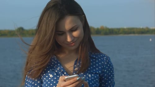 Woman Using Smartphone by Lake on a Sunny Day