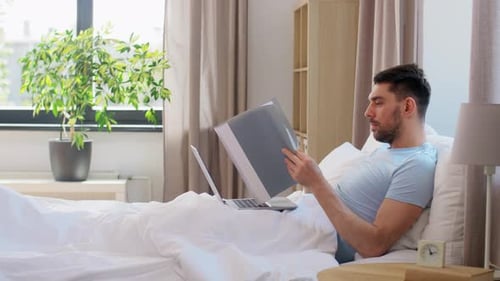 Man Working On Laptop While Lying in Bed