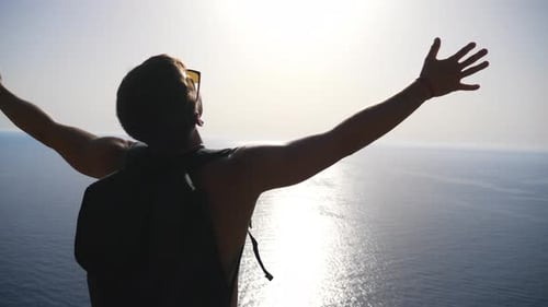 Male Hiker with Backpack Reaching Up Peak and Raising His Hands Admiring Scenic Seascape
