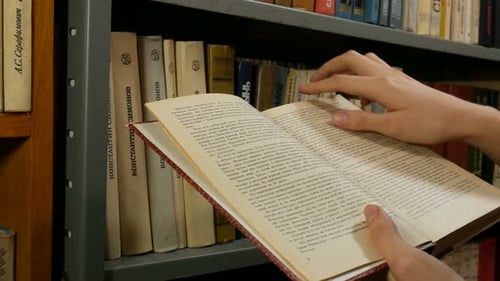 Mädchen blättert Bücherseiten vor dem Regal um
