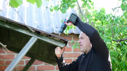 Man Repairs Canopy of an Old Small House