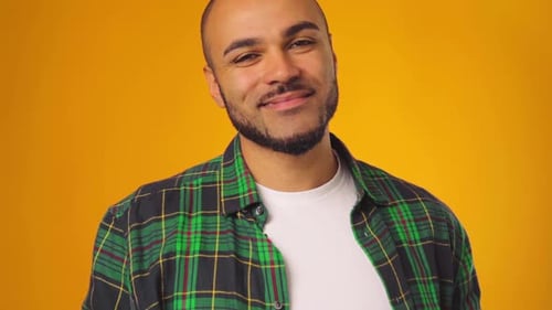 Jovem afro-americano em camisa casual sorrindo e levantando as sobrancelhas contra fundo amarelo