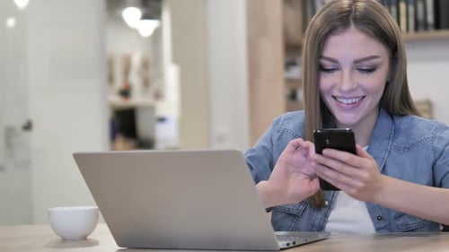 Young Woman Using Smartphone at Desk With Laptop