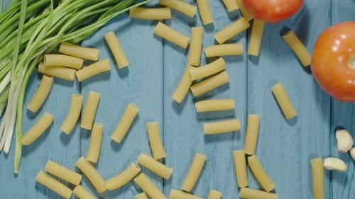 Tortiglioni Pasta Rolling On The Blue Wood Table, Frühlingszwiebeln, Tomate