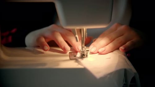Woman's Hands Guiding Fabric Through Sewing Machine