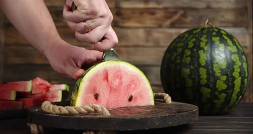 Male Hand with Knife Cut Half of the Watermelon To Pieces.